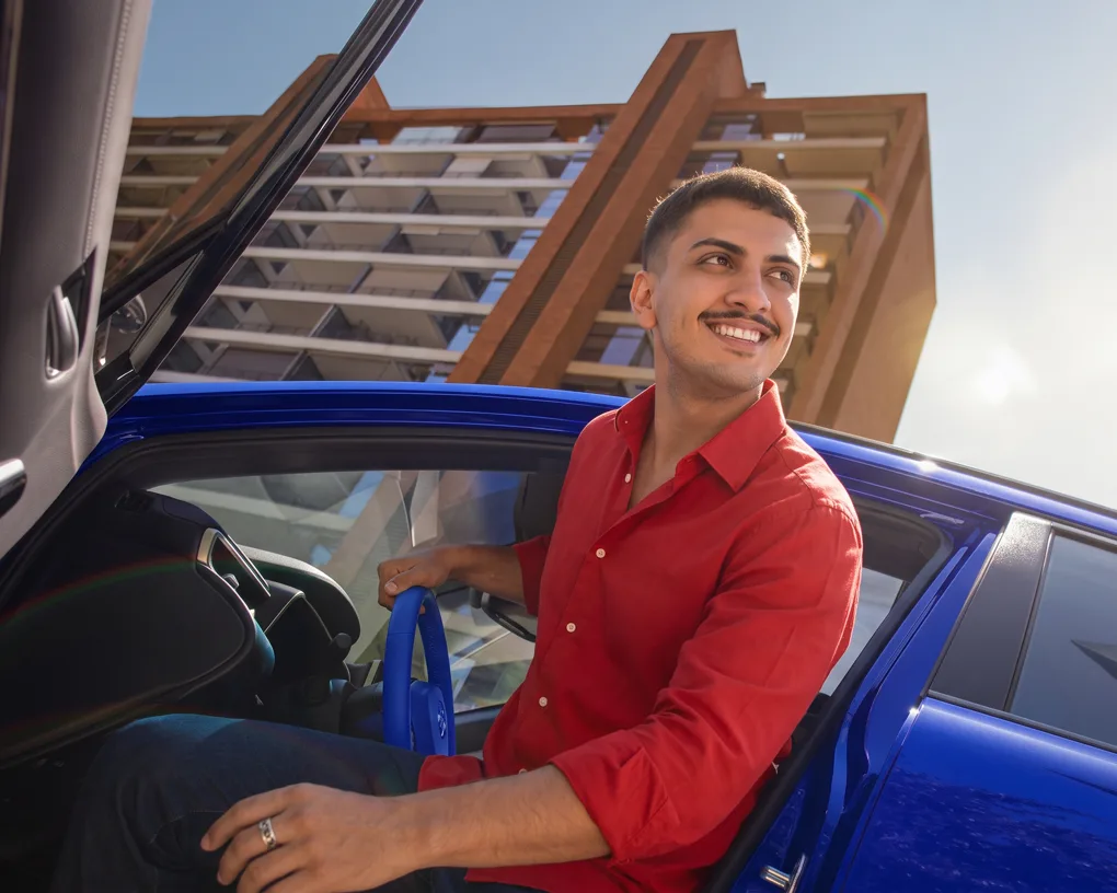 Homem sorrindo sentado no carro azul, de camisa vermelha